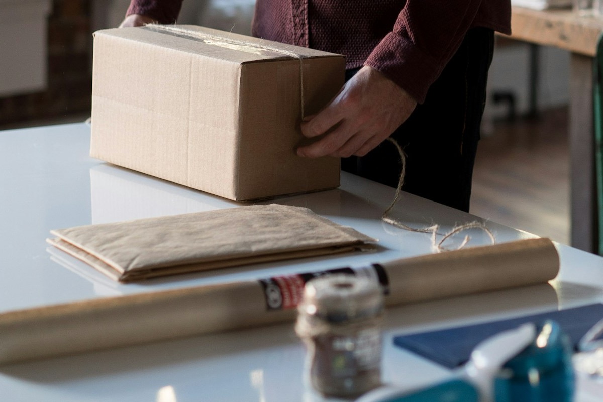 Hands tying up a shipping box on a counter beside kraft paper